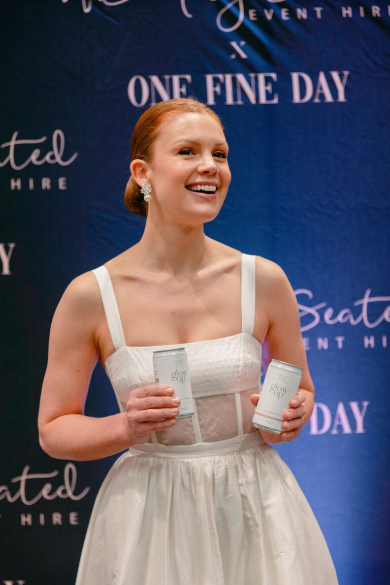 A woman smiling, holding two canned drinks.