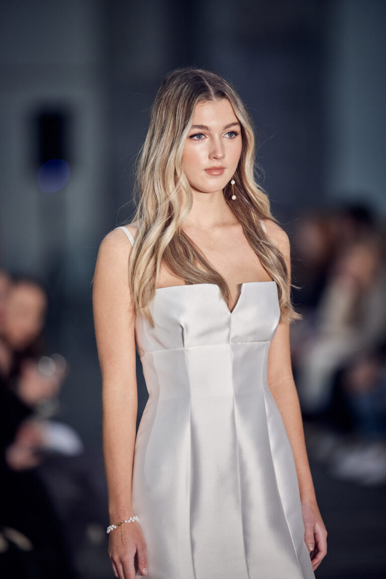 A woman in a white wedding gown walking on a fashion show runway.