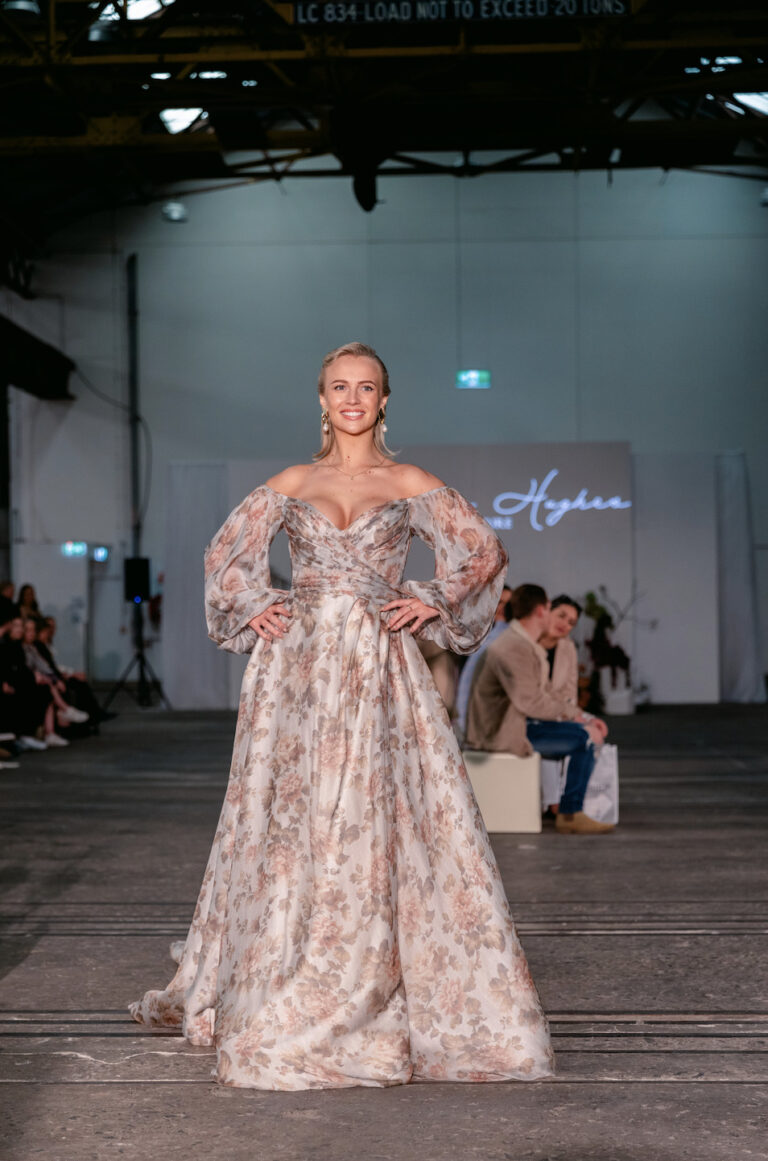 A woman in a light floral dress walking on a fashion show runway.
