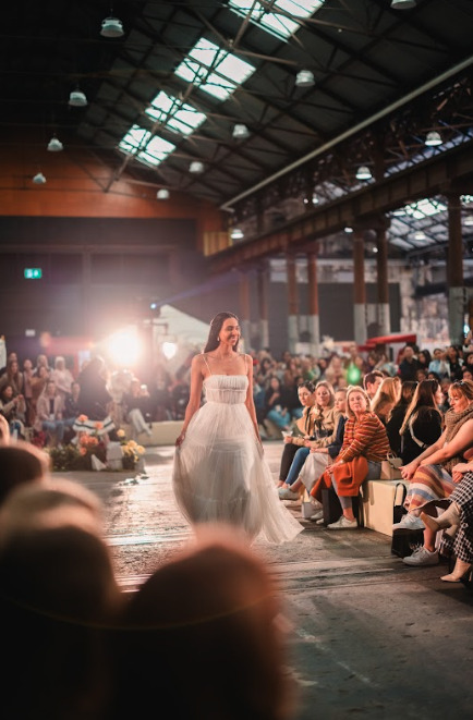 A woman in a white wedding gown walking on a fashion show runway.