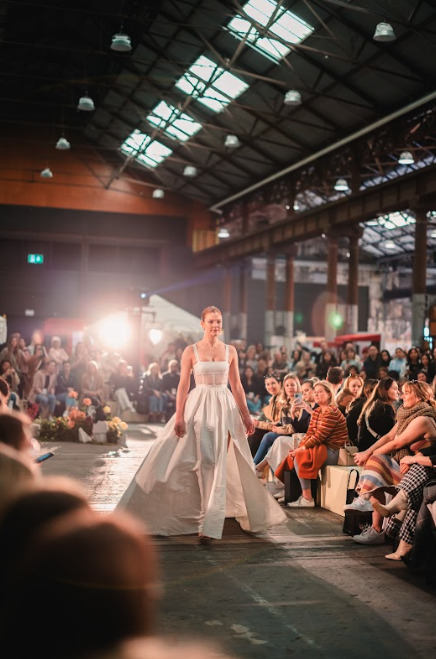 A woman in a white wedding gown walking on a fashion show runway.