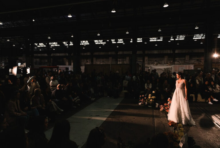 A woman in a white wedding gown walking on a fashion show runway.
