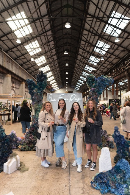 Four women posing in front of a sign that says "One Fine Day".