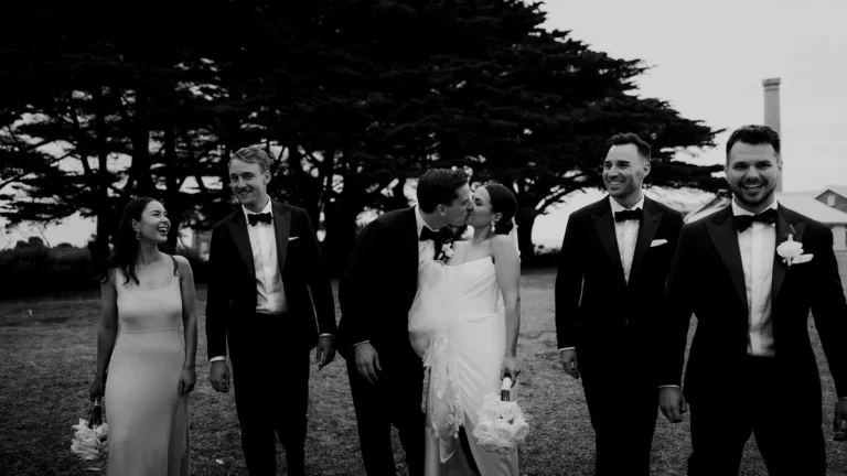 Groom and groomsmen dressed in Oscar Hunt Men's Tailored Wedding Suits in Melbourne, capturing a romantic kiss with the bride.