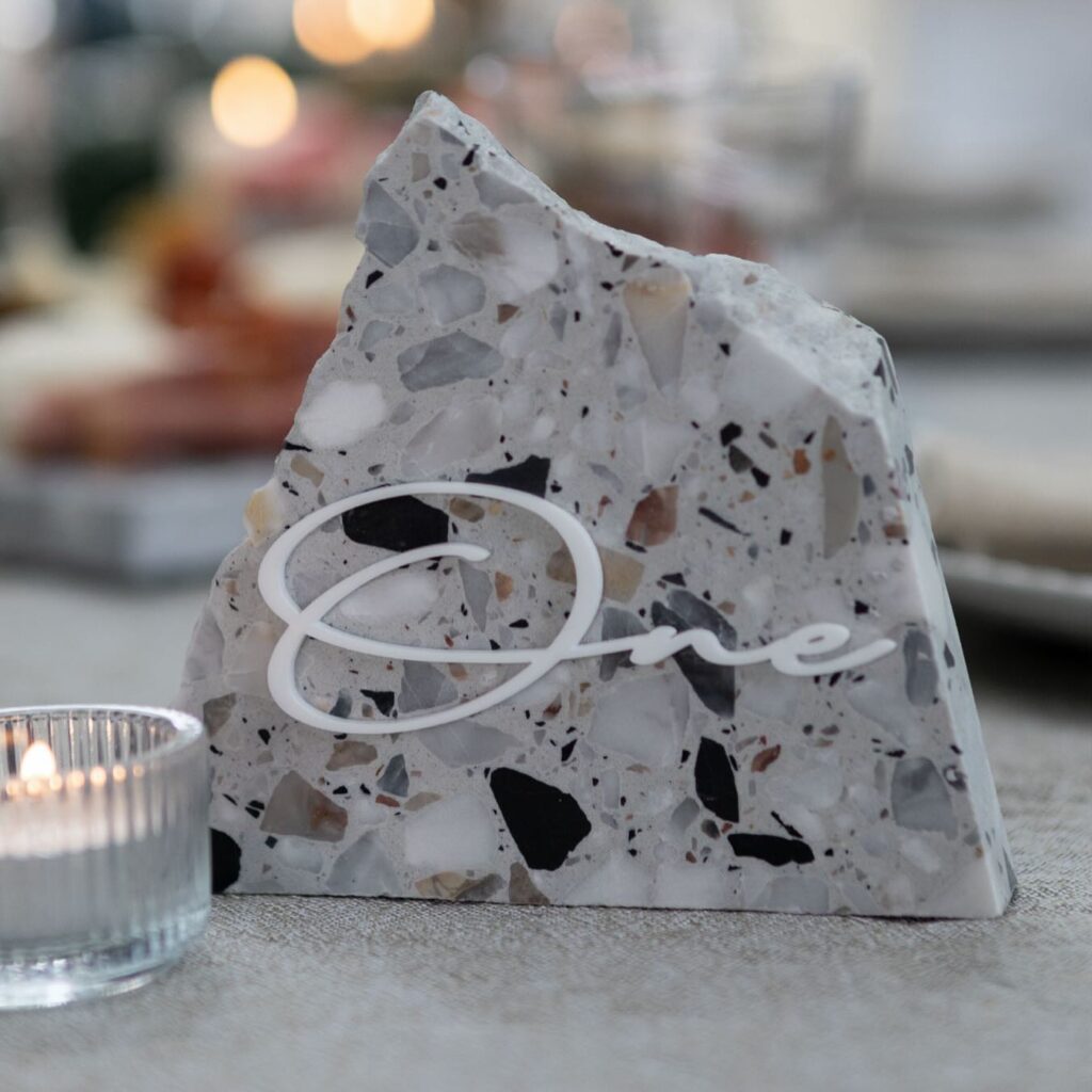 Stone table with a lit candle and a table number sign reading "one," styled by Insieme Homewares, best wedding event hire Melbourne.