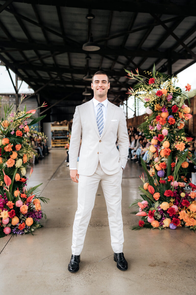A man in a suit and tie standing in front of colorful flowers.