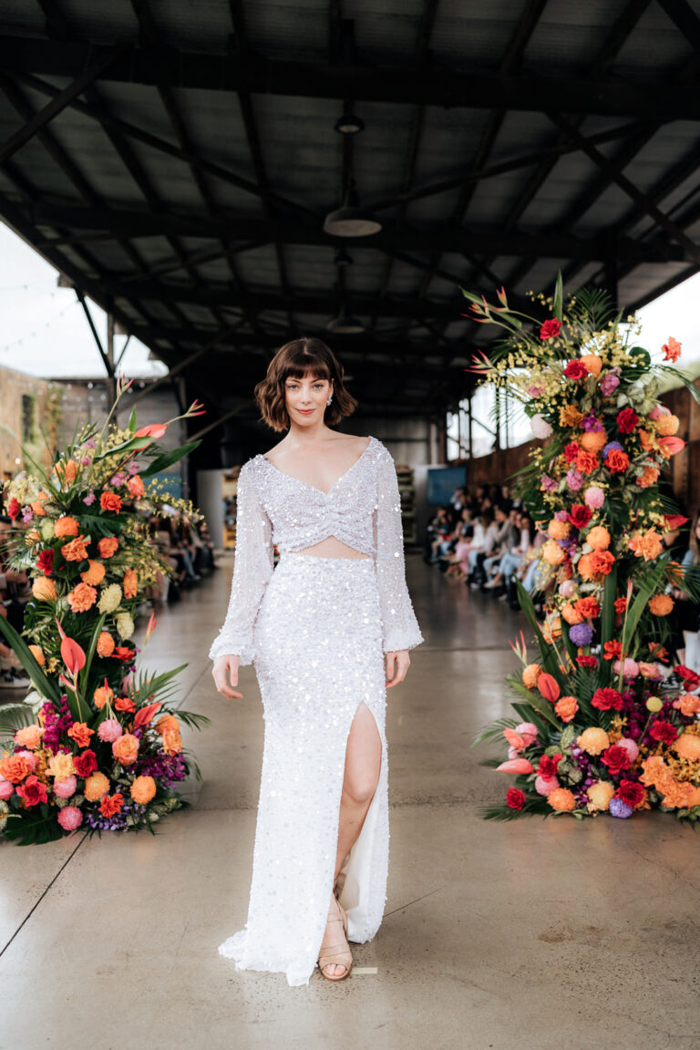 A woman in a white dress with a high slit skirt struts down the runway during a fashion show.