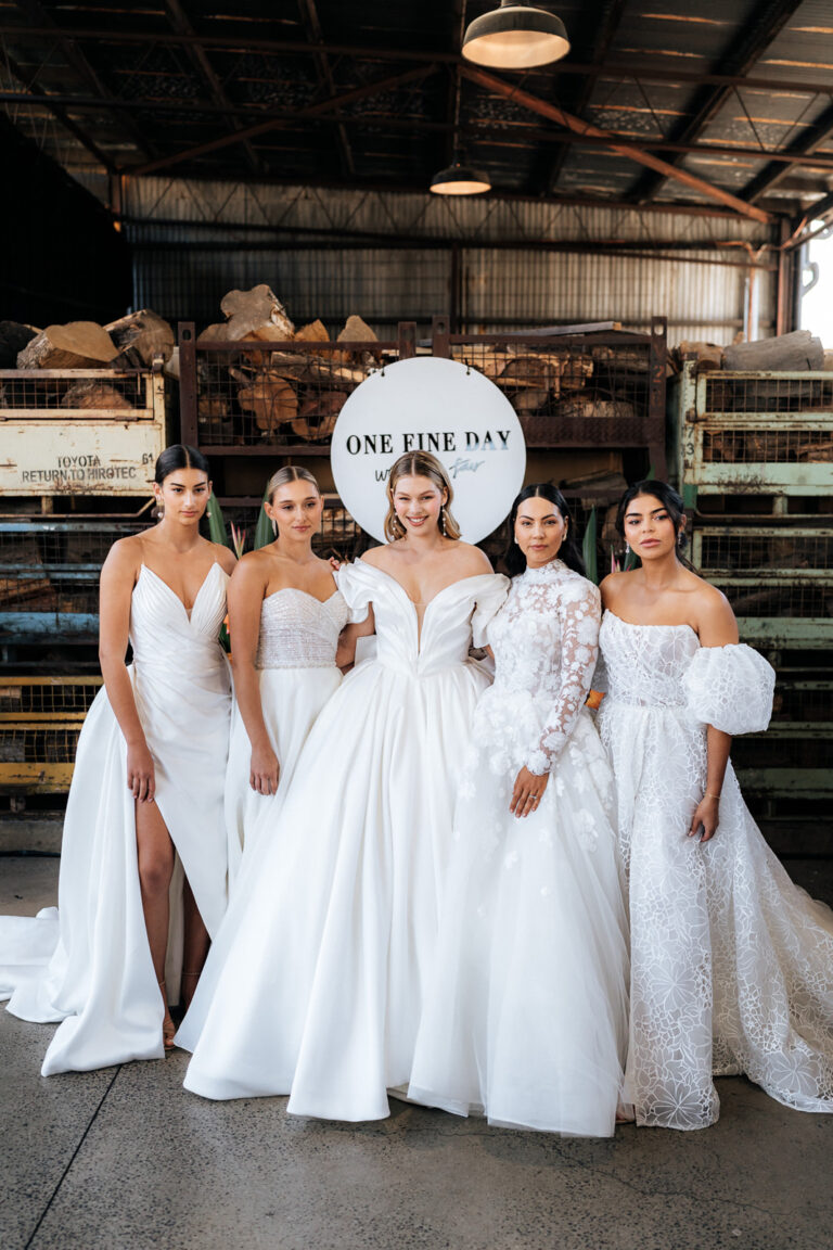 Four bridesmaids in white dresses posing in front of a sign at a wedding.