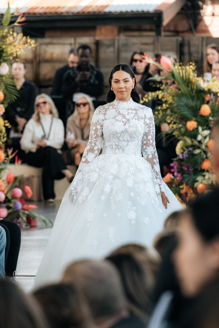 A bride in a wedding gown gracefully walks down the runway, radiating elegance and joy.