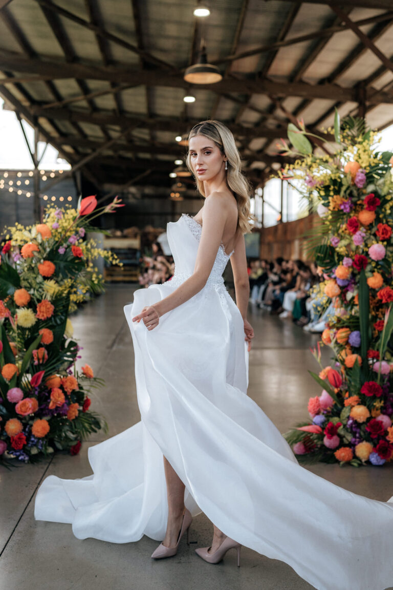 A bride in a white gown walking under a floral archway.