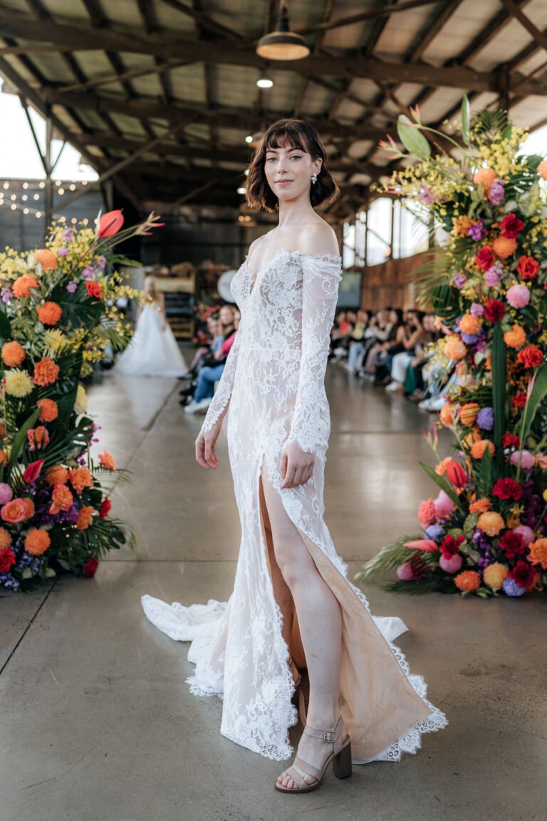 A bride in a wedding gown posing in front of beautiful flowers.
