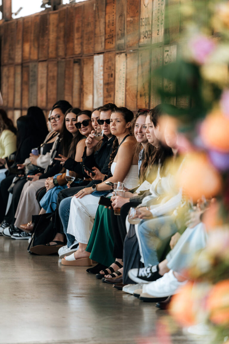 A row of people sitting at a fashion show, watching models on a runway.