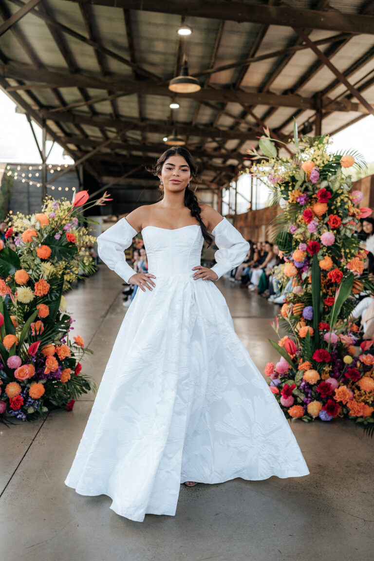 A bride in a white wedding gown posing in front of beautiful flowers.