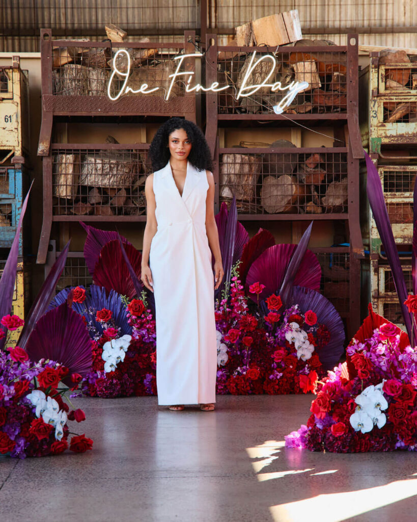 Model in a sleeveless white bridal gown walking at a bridal runway show in Melbourne with vibrant floral backdrop.