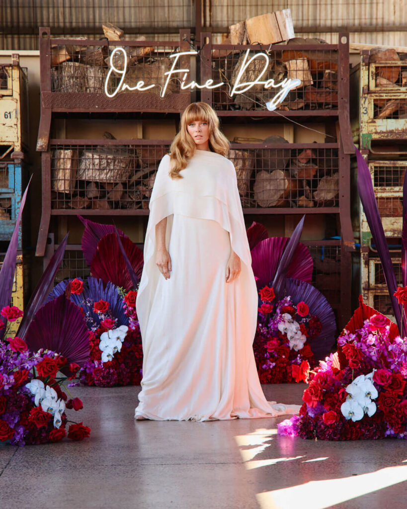 Melbourne bridal runway show featuring a model in a long white cape-style wedding gown with colorful floral arrangements.