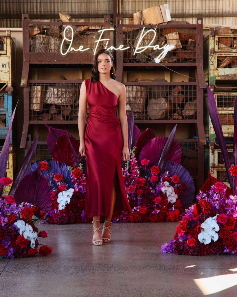 Bridal runway show in Melbourne featuring a model in a striking red satin one-shoulder bridal gown with thigh-high slit.
