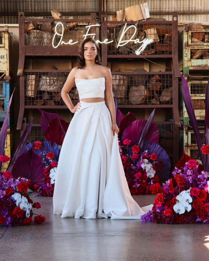 Model posing in a white two-piece simple wedding dress with strapless top and floor-length skirt at a bridal runway show in Melbourne.