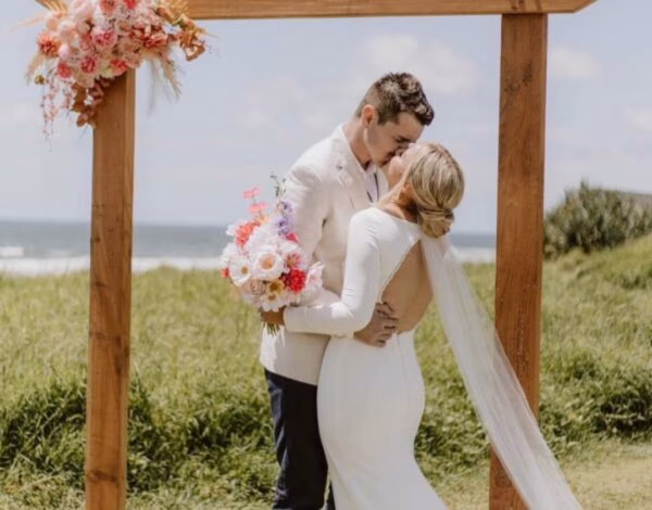 Florists Listing Category Gather Botanical Bride and groom sharing a sweet moment with silk floral arrangement backdrop by Gather Botanical