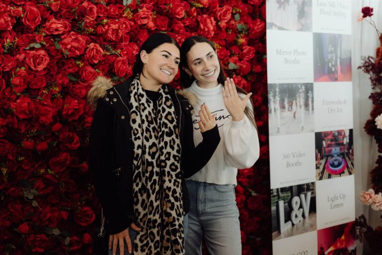 Two visitors posing in front of rose design backdrop at wedding expo in Sydney 2025