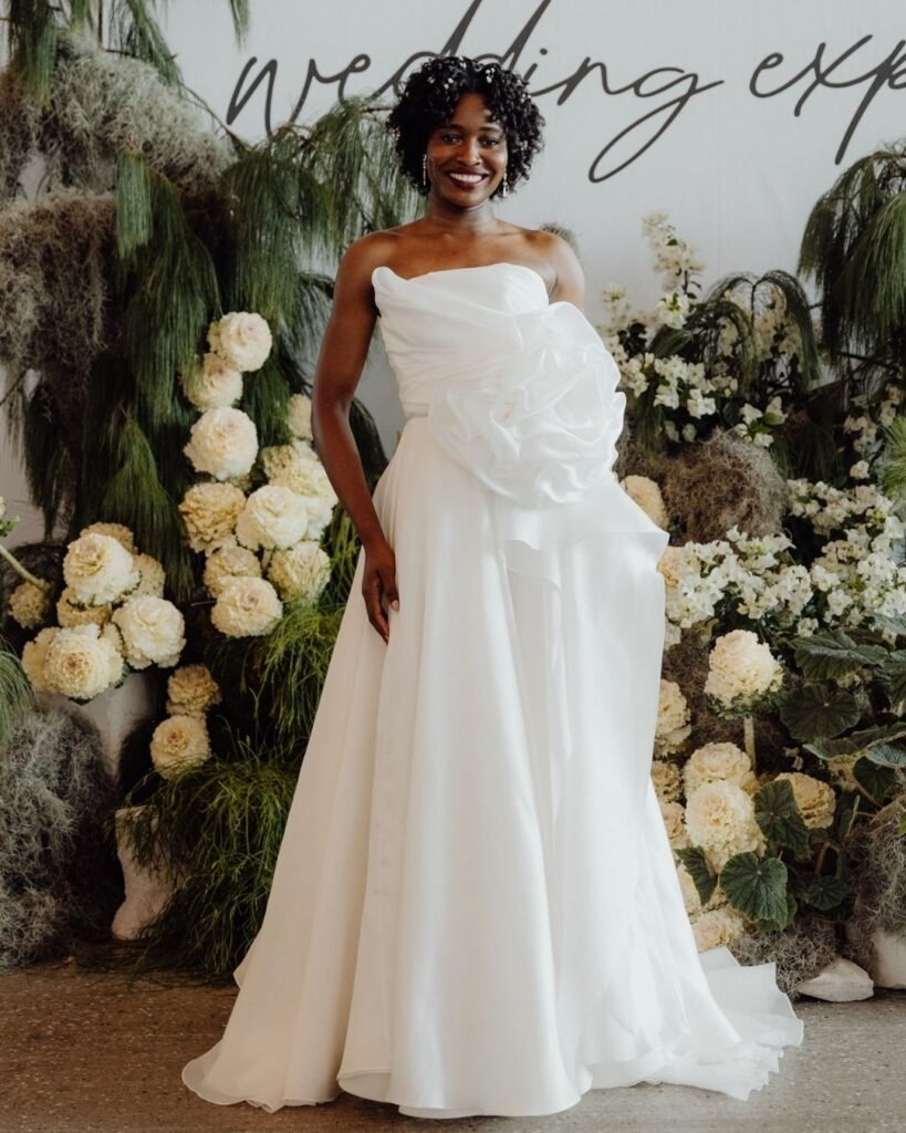 Model wearing tube-style satin dress with big rose detail on the side at bridal runway show in Sydney 2025