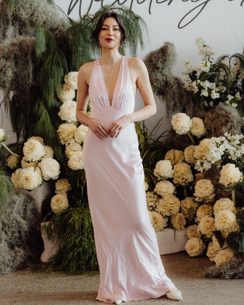 Model showcasing fitted light pink satin dress with deep V-line bodice at bridal runway show in Sydney 2025