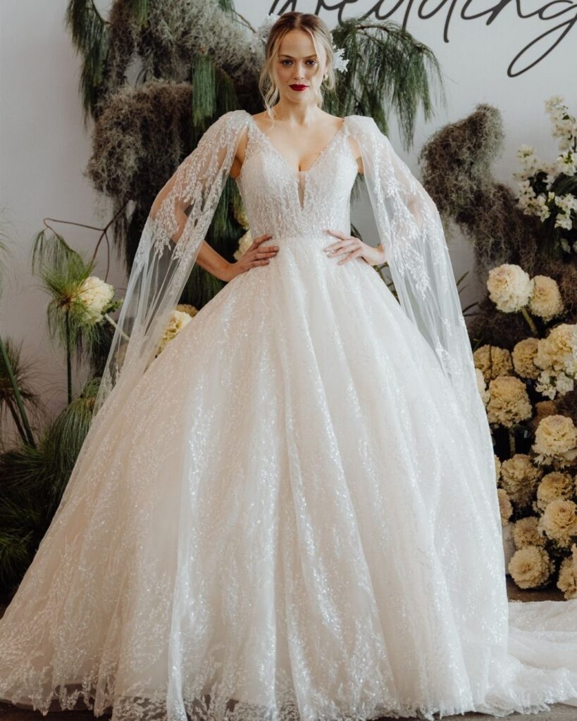 Model wearing ball gown chiffon dress with elegant long fabric detail on shoulder at bridal runway show in Sydney 2025