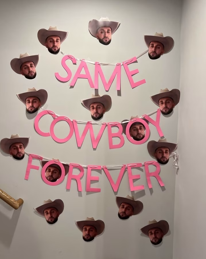 The words "same cowboy forever" strung up across cut outs of a grooms face at a bachelorette party