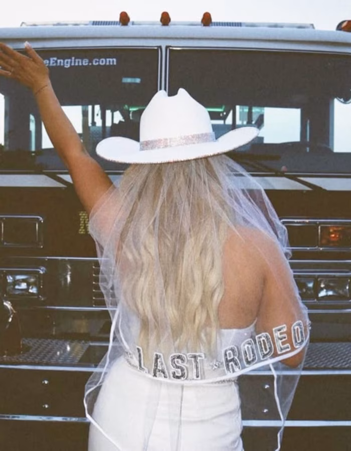 A bride facing away from the camera in a white cowboy hat with a veil attached