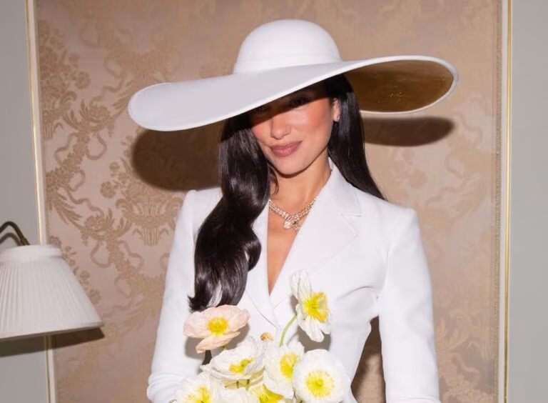 Dua Lipa's wedding style, a large brimmed white hat shadowing her face, and a fitted blazer.