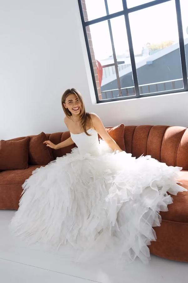 A Sydney bride laughing on a couch in a bridal boutique, wearing a wedding dress