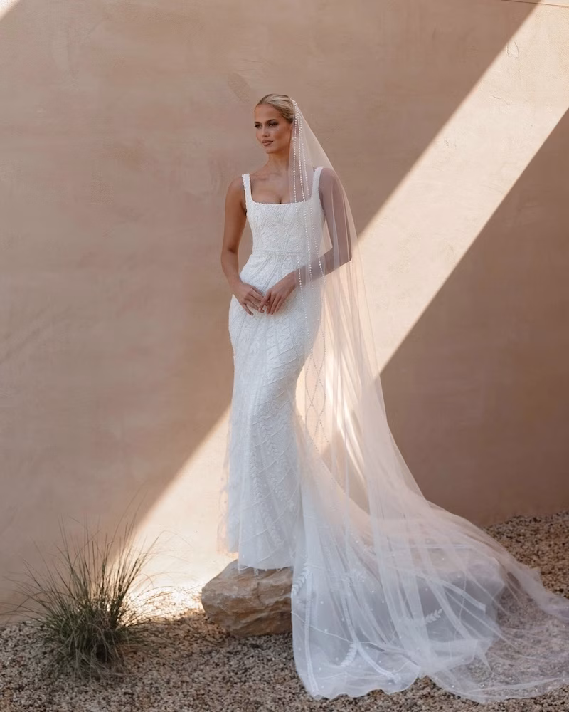 A bride in a cathedral veil standing in front of a beige wall