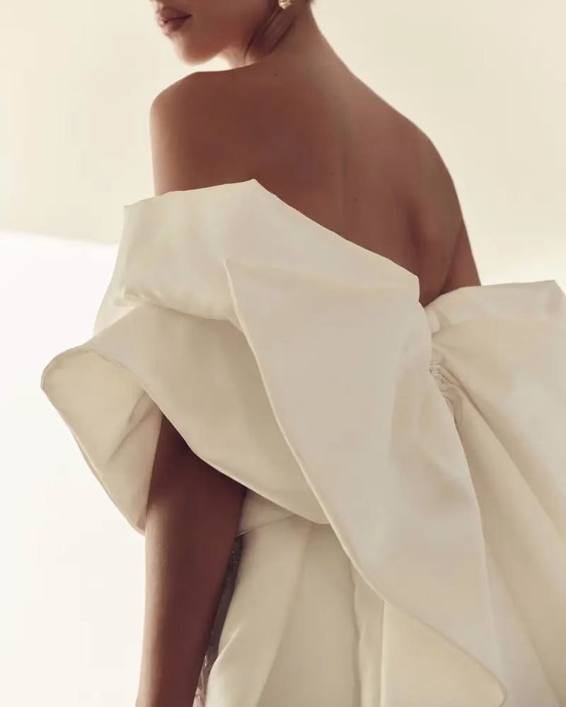 A bride with her back facing the camera wearing bridal accessory of 2026, a bow cape