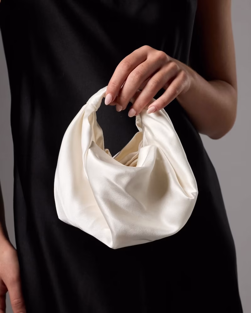A woman holding a silk white clutch bag
