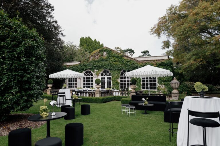 A wedding event set up with black furniture and white umbrellas in a garden