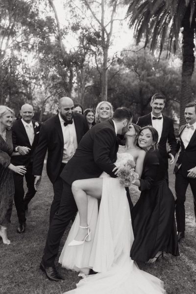 A wedding party poses for a photo with the bride and groom, smiling and looking happy.