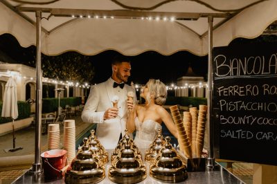 A couple at an ice cream cart holding ice cream cones.