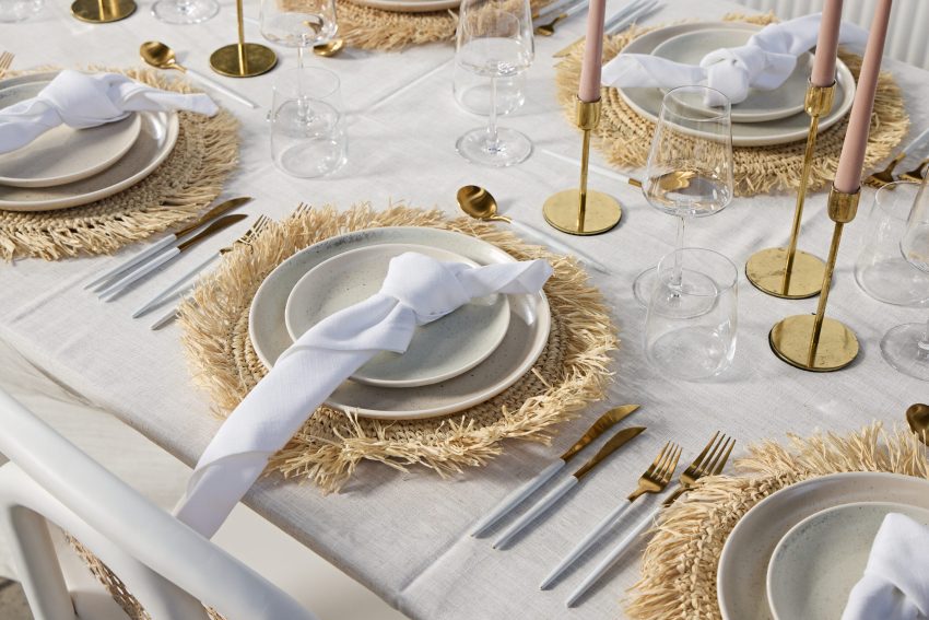 A table set with white and gold plates, silverware, and glasses.