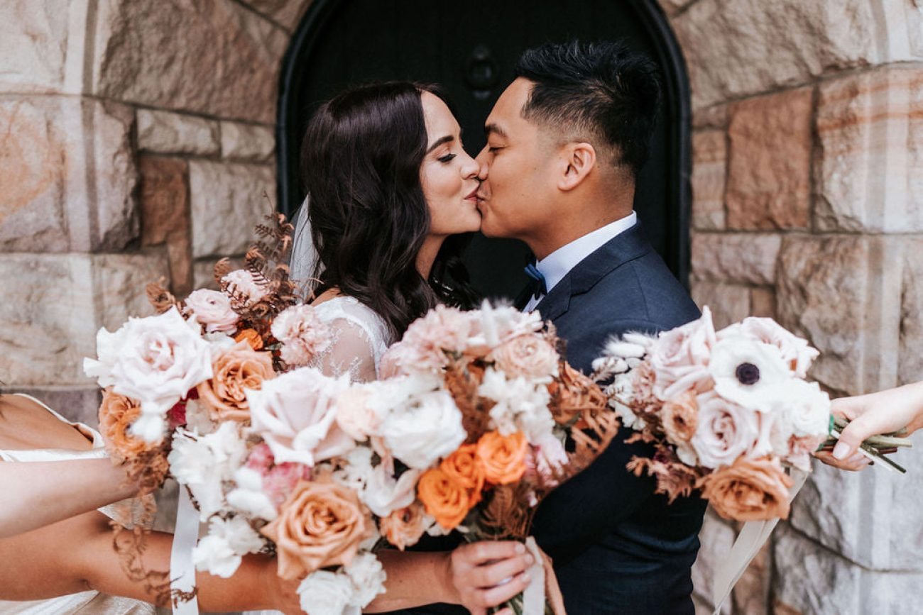 a bride and groom kissing in front of a stone building