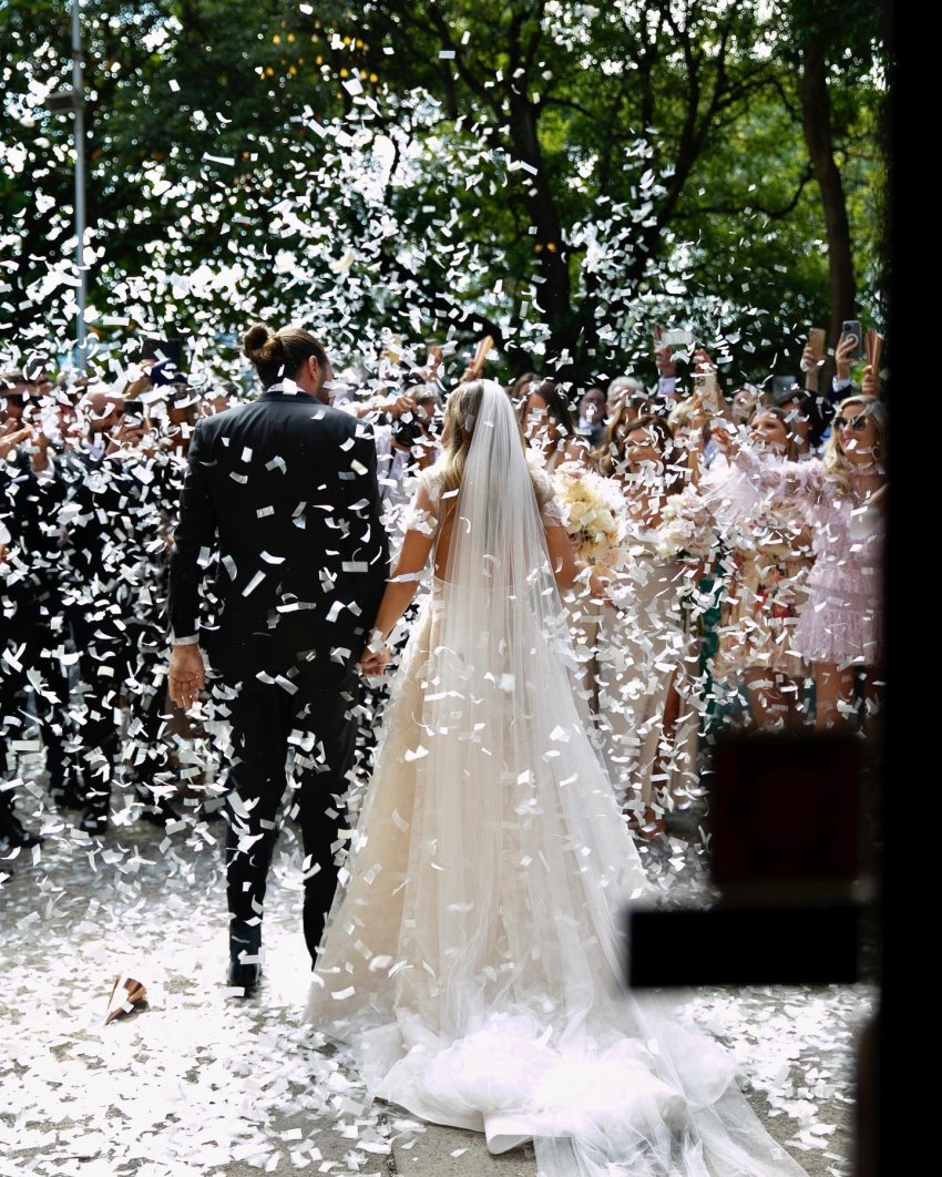 A bride and groom walking down the aisle with confetti falling around them.