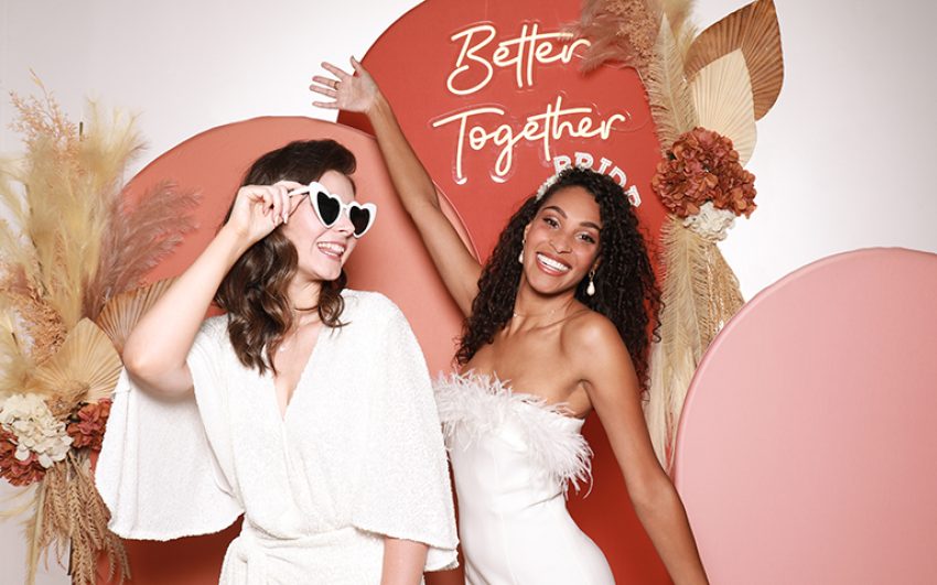 Two women in white dresses smiling at the camera.