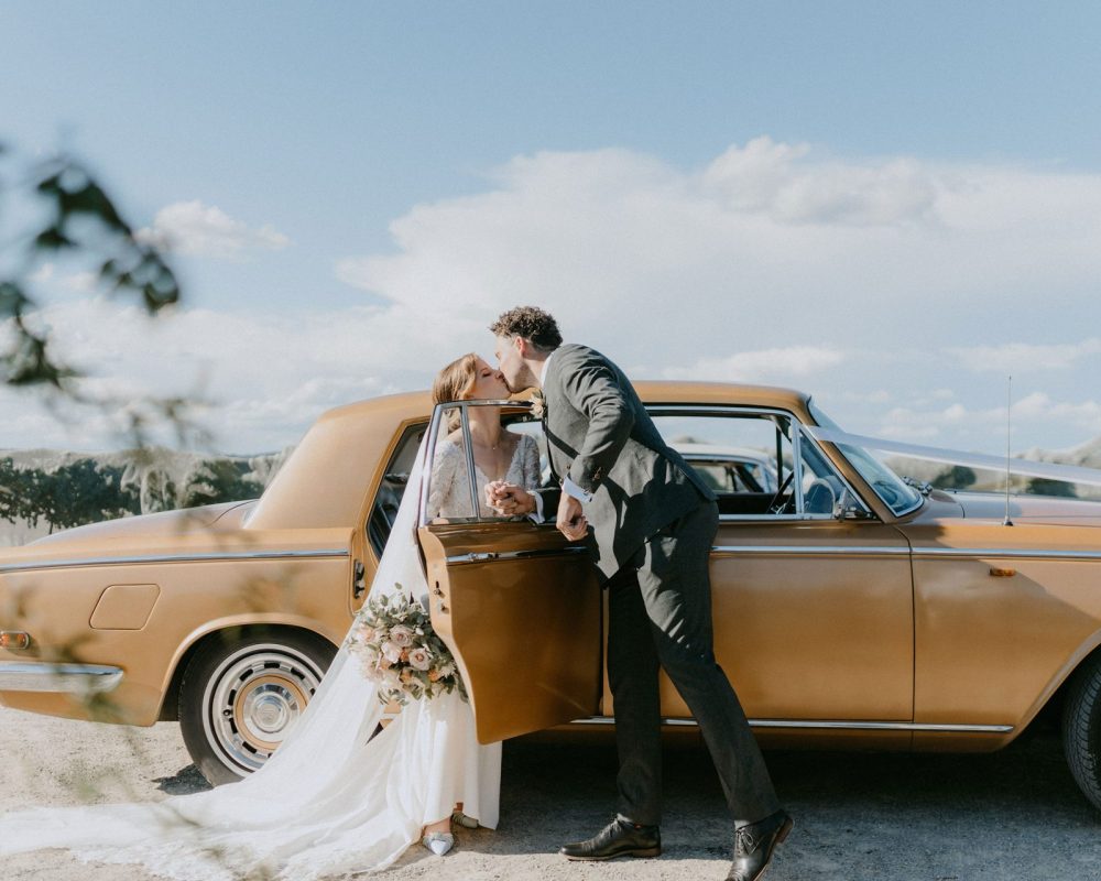 groom kissing bride as she emerges from vintage car