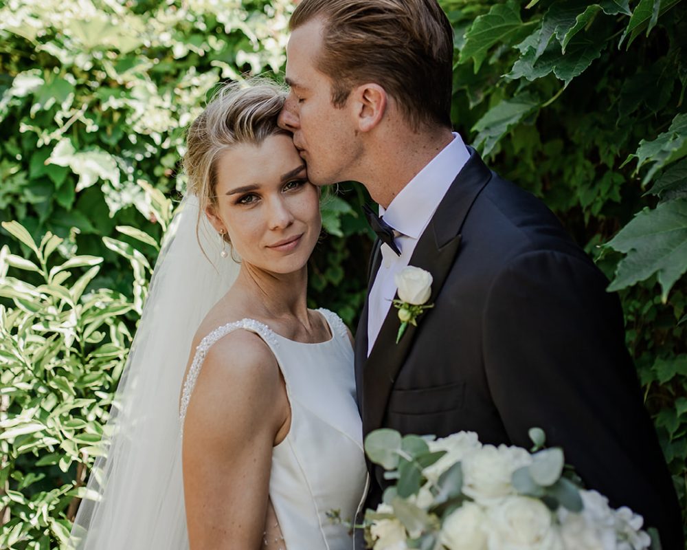Bride looking straight as the groom kisses her cheek, captured by The Amour Collective Sydney Wedding Photographer.