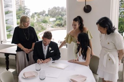 A man and woman signing a wedding certificate in front of a group of people.