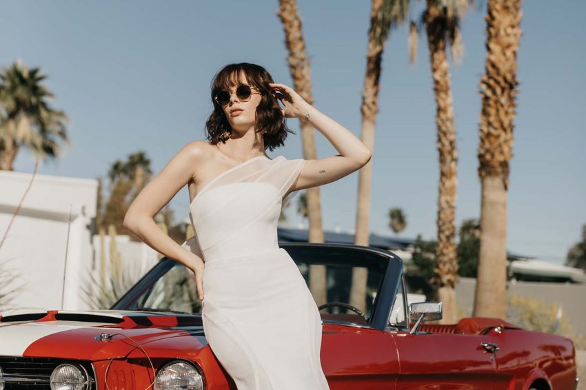 sexy unconventional wedding dress worn by a model sitting infront of a vintage car