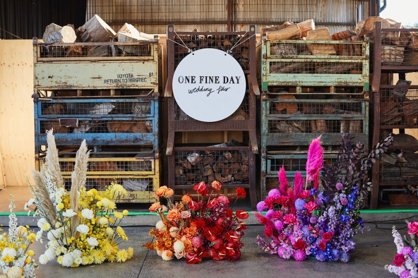 A colorful array of flowers arranged in a warehouse, creating a vibrant and lively display and a sign that says 