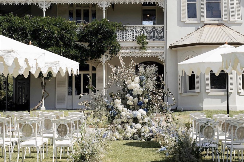 A wedding ceremony outdoors with white chairs and umbrellas set up for guests.