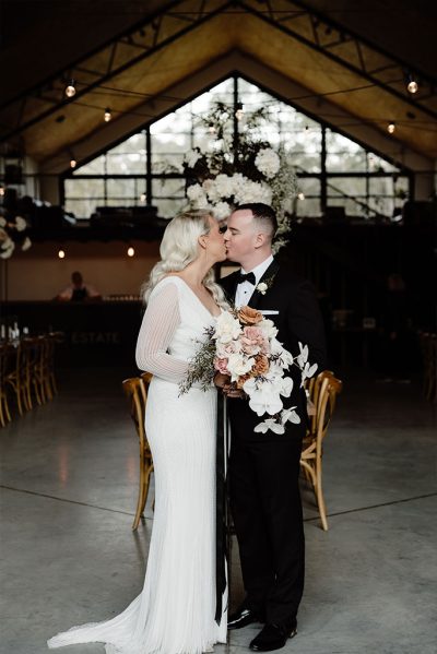 A couple kissing while holding a bouquet of flowers.